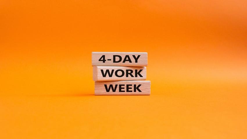 Holzwürfel mit Schrift "4 Day Work Week" auf orangem Hiuntergrund